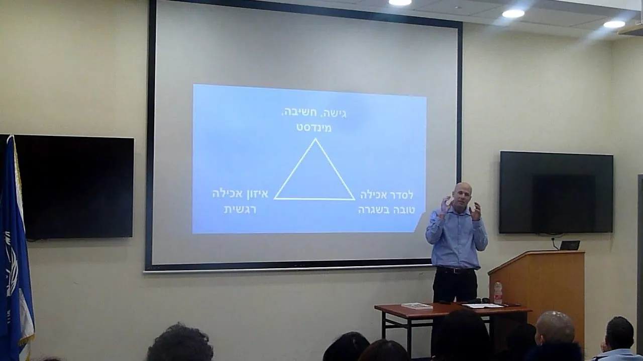 רואי מציג את משולש המצוינות בהרצאה